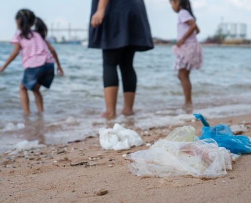 Garbage on the beach with family playing water in the sea on background, environmental pollution of tropical sea